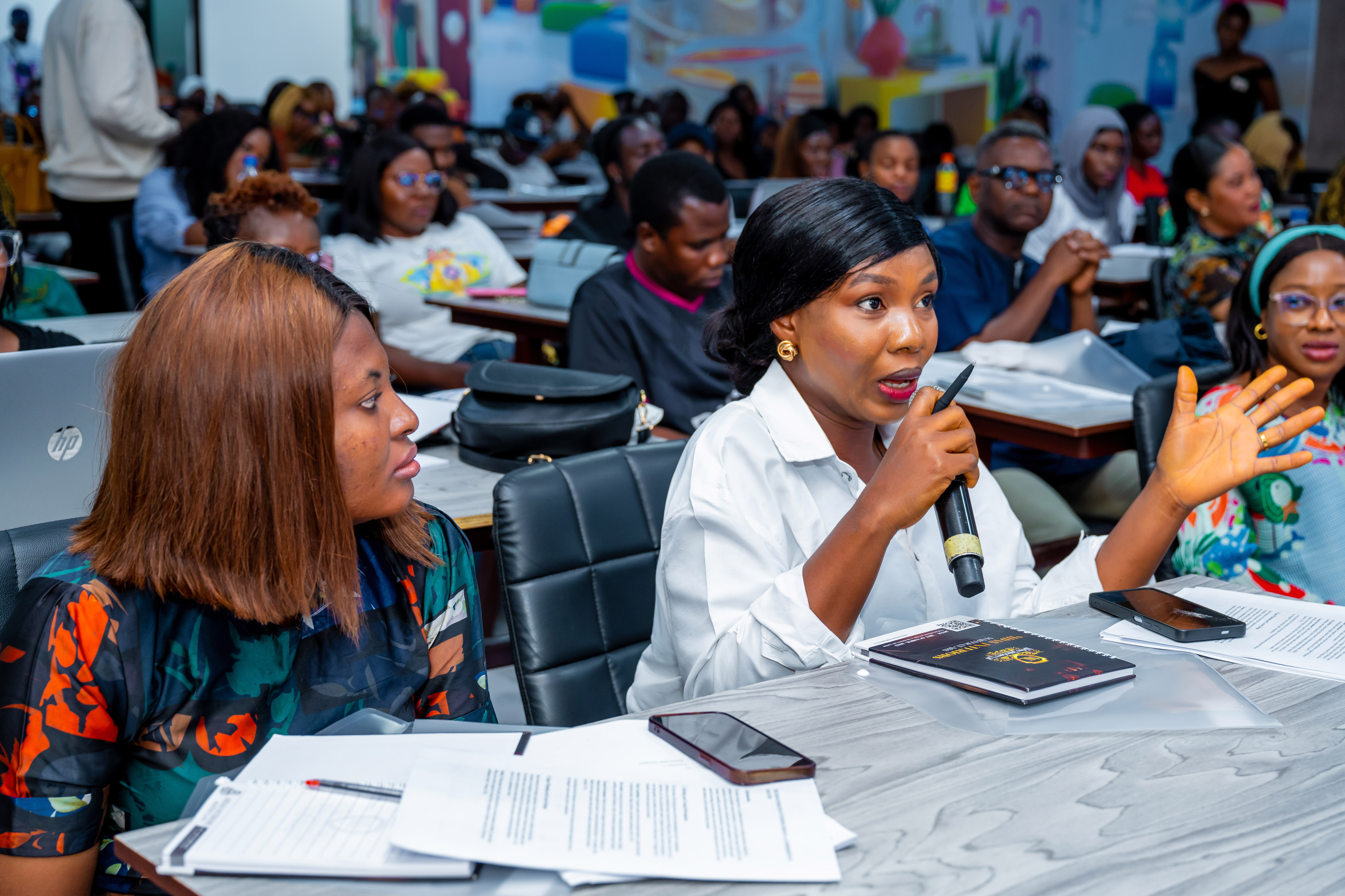 Woman speaking into a microphone with expressive hand gesturing during a classroom discussion.