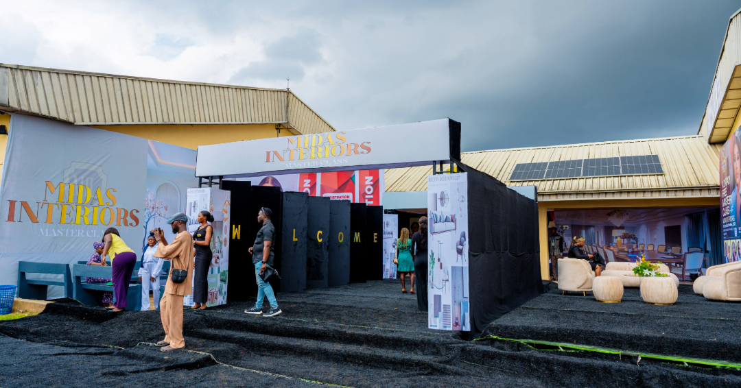 People gathered outside a Midas Interiors Masterclass event booth with black flooring and banners, under a cloudy sky.