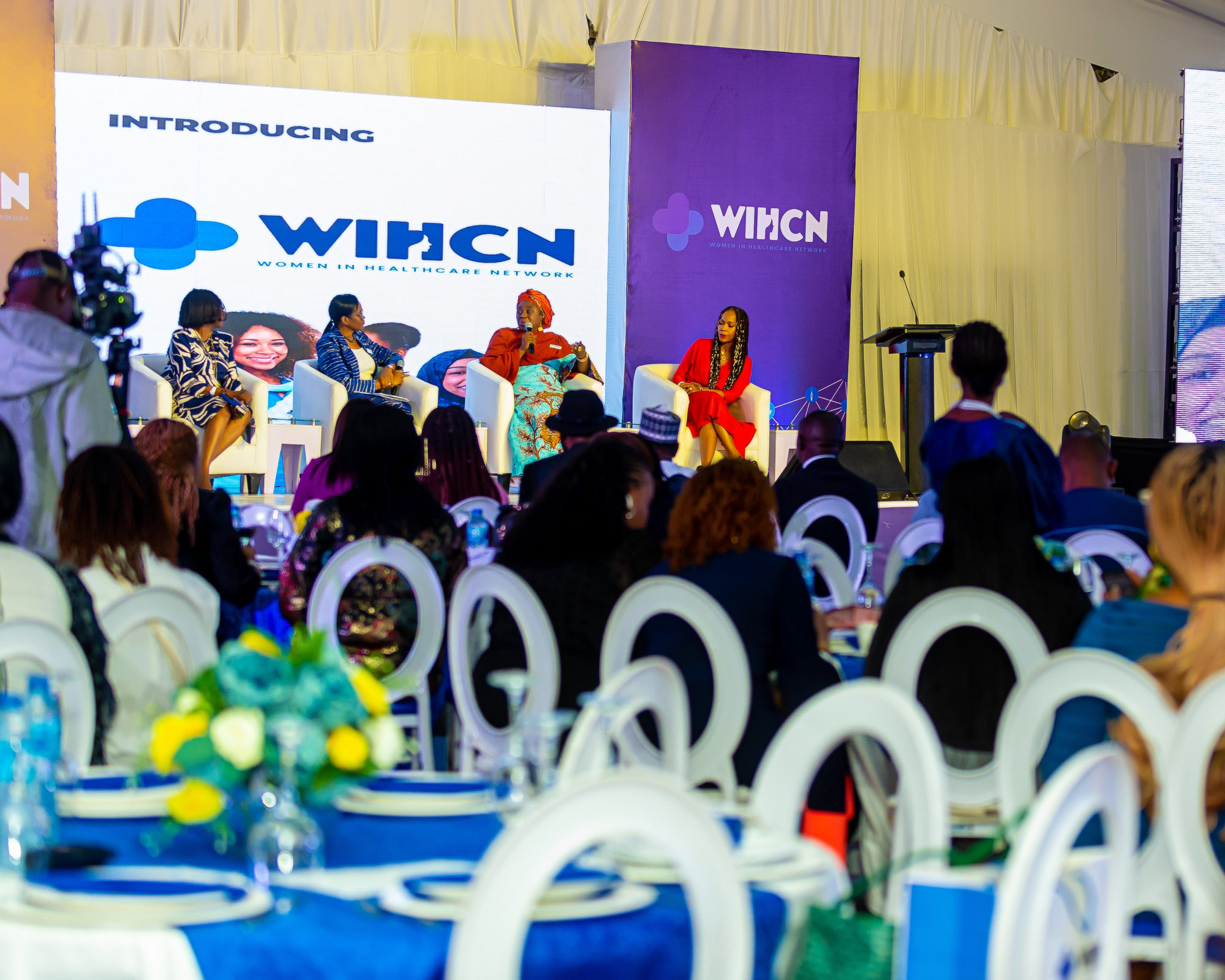 Panel of four women seated on stage speaking at a Women in Healthcare Network event with audience in foreground.