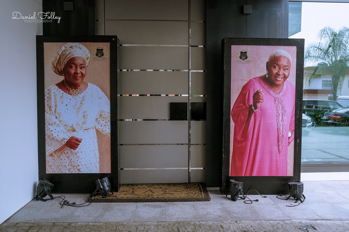Two large vertical portraits of elderly women in traditional attire, displayed on either side of a modern glass door entry.